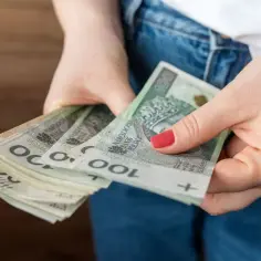 Dłonie trzymające stos banknotów 100 zł. Czy to już kwota bazowa służba cywilna 2026?