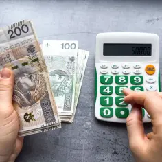Dłonie liczą polskie banknoty 200 i 100 zł obok kalkulatora z wyświetloną kwotą 50000. Czy to prognoza płacy minimalnej 2026?