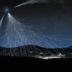 Nocne niebo nad górami, gdzie rozchodzą się świetliste ścieżki, symbolizujące **promieniowanie kosmiczne** uderzające w atmosferę.
