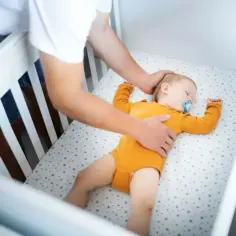 Ojciec kładzie śpiące dziecko do łóżeczka. Ile śpi noworodek? To pytanie nurtuje wielu rodziców.