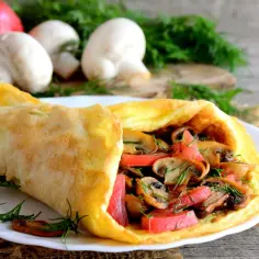 Puszysty omlet z pieczarkami i pomidorami, udekorowany koperkiem.