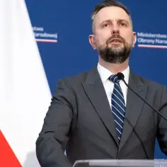 Minister obrony narodowej przemawia na tle flagi Polski i logo ministerstwa.