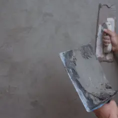 Ręce zacierają tynk na ścianie ze styropianu. Proces jak tynkować styropian, tworząc gładką powierzchnię.