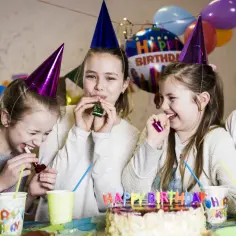 Radość na 10 urodziny w domu! Cztery dziewczynki w czapkach urodzinowych dmuchają w gwizdki, świętując wesoło.