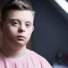 Chłopiec z zespołem Downa w różowej koszulce. Czy osoby z zespołem Downa mogą mieć dzieci? Tak, to możliwe.