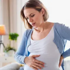 Ciężarna kobieta trzyma się za brzuch i plecy, odczuwając ból żeber w ciąży.