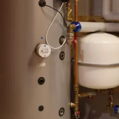 Uszkodzone naczynie przeponowe objawy: widoczny bojler, biały zbiornik przeponowy i rury instalacji grzewczej.