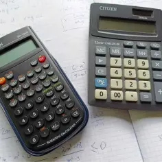 Dwa kalkulatory leżą na kartkach z zadaniami matematycznymi. Czy na egzaminie ósmoklasisty można mieć kalkulator? Tak, ale tylko prosty.