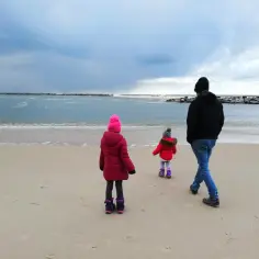 Rodzina spaceruje po plaży zimą. Gdzie nad morze z dzieckiem zimą? Tu! Wiatr i fale tworzą chłodną atmosferę.