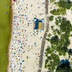 Tłum ludzi na piaszczystej plaży, kąpielisko i zielone drzewa. To widok z lotu ptaka, który pokazuje, że Litwa ma dostęp do morza.