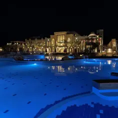 Nocny widok na hotel Lazuli z oświetlonym basenem i palmami.