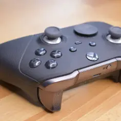 Czarny kontroler Xbox One leży na drewnianym blacie. Dowiedz się, jak podłączyć pada do Xboxa One, aby rozpocząć grę.