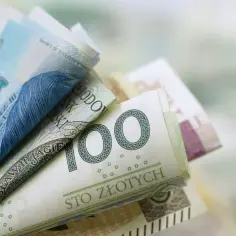 Stos polskich banknotów, w tym 100 zł, symbolizujący zasilek pielegnacyjny.