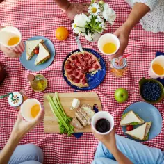 Radosny piknik z pysznym jedzeniem: kanapki, ciasto z truskawkami, owoce, warzywa i napoje. Wszyscy cieszą się wspólnym posiłkiem na czerwonym kocu.