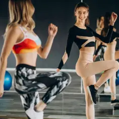 Dwie kobiety ćwiczą w sali gimnastycznej, wykonując ćwiczenia na stepie. Ich ruchy świadczą o zaangażowaniu w trening total body conditioning.