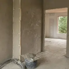 Ściany pokryte tynkami cementowo wapiennymi, przygotowane do dalszych prac. W kadrze wiadro z zaprawą i narzędzia.