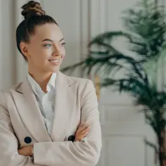 Uśmiechnięta kobieta w beżowej marynarce, z włosami upiętymi w kok. Zastanawia się, co trzeba zrobić, żeby zostać psychologiem.