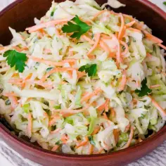 Klasyczna surówka coleslaw z kapusty i marchewki w drewnianej misce, udekorowana natką pietruszki.