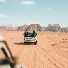 Ludzie podróżują pickupem Toyota przez pustynię Wadi Rum w Jordanii. Odpowiedź na pytanie: czy w Jordanii jest bezpiecznie? Tak, podróżowanie po Jordanii jest bezpieczne.