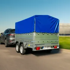 Ciemnoszary SUV ciągnie przyczepkę z niebieską plandeką. Zastanawiasz się, ile kosztuje przegląd przyczepki?