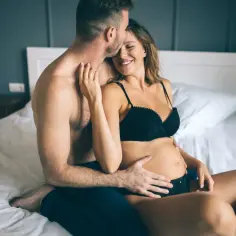 Czuły pocałunek na czole ciężarnej kobiety. Intymne chwile i bliskość, odkrywające komfortowe pozycje seksualne w ciąży.