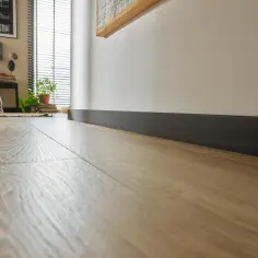 Nowoczesne wnętrze z jasną podłogą i ciemnymi dębowymi listwami przypodłogowymi, które podkreślają elegancję pomieszczenia.