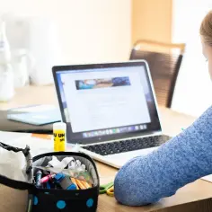 Dziewczynka przy laptopie, otwarte piórnik z przyborami, klej. Analiza danych, big data w nauce.