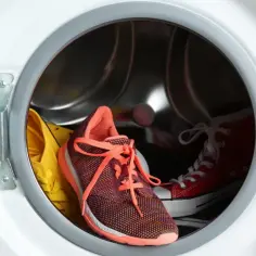 Czy pranie butów sportowych w pralce trwale uszkadza ich konstrukcję? W bębnie pralki kolorowe trampki i buty sportowe czekają na cykl.