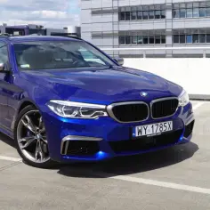 Błękitne BMW 550d kombi na parkingu przed nowoczesnym budynkiem.