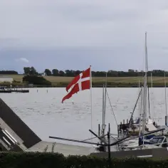Dania graniczy z Niemcami. Flaga Danii powiewa nad portem pełnym żaglówek.