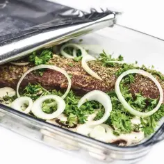 Mięso w naczyniu żaroodpornym, przykryte folią aluminiową, z cebulą i ziołami.