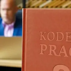 Mężczyzna w garniturze przegląda dokumenty przy biurku, obok stoi oprawiony "Kodeks Pracy", który przypomina o jego uchwaleniu.
