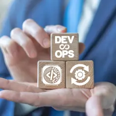 Dłonie trzymają drewniane klocki z symbolami DevOps, kodowania i ciągłego cyklu. To wizualizacja osiągania szczytów w rozwoju oprogramowania.