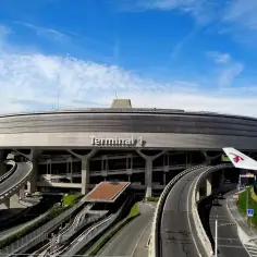 Lotnisko w Paryżu, Terminal 1, z charakterystyczną, okrągłą architekturą i drogami prowadzącymi do niego. W tle widać skrzydło samolotu.