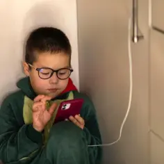 Chłopiec w okularach i piżamie próbuje dowiedzieć się, jak wyłączyć blokadę rodzicielską w telefonie, grając na nim.