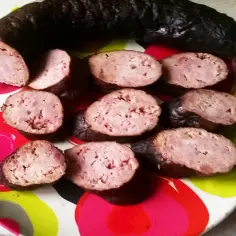 Kiełbasa wędzona na gorąco, pokrojona w plastry, ułożona na kolorowym talerzu.