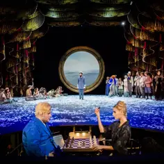 Na dużej scenie Teatru Capitol trwa spektakl. Aktorzy w strojach z epoki, wśród nich kapitan, siedzą na scenie usypanej płatkami.