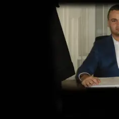 Mężczyzna w garniturze siedzi przy biurku z dokumentami.