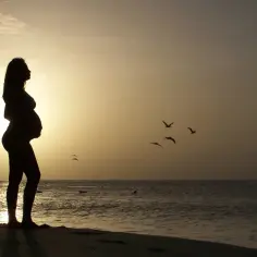 Ciężarna kobieta na plaży o zachodzie słońca. Idealne miejsce, gdzie na wakacje w ciąży w Polsce.