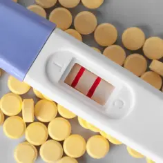 Test ciążowy z dwoma czerwonymi paskami leży wśród żółtych tabletek, być może suplementów z kwasem foliowym.