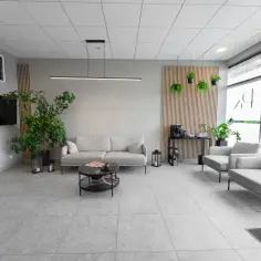 Nowoczesna poczekalnia kliniki z sofami, fotelami, roślinami i kawomatem.