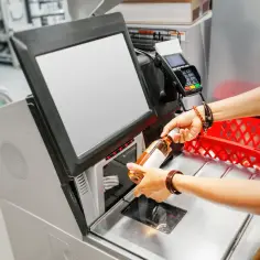 Kasa samoobsługowa: skutki automatyzacji handlu a zatrudnienie. Klient skanuje butelkę, zastanawiając się nad przyszłością pracy kasjerów.