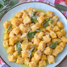 Pyszne gnocchi z dyni, polane masłem z szałwią i posypane parmezanem, wyglądają apetycznie na talerzu.