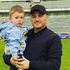 Piotr Nalepa z synkiem na stadionie. Chłopiec w niebieskiej kurtce z zabawnymi wzorami.