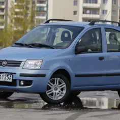 Niebieski fiat panda automat z relingami dachowymi, zaparkowany na mokrym asfalcie.