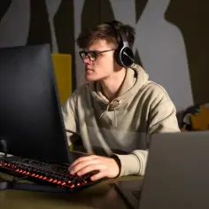 Młody technik programista w okularach i słuchawkach pracuje przy komputerze.