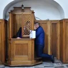 Mężczyzna klęczy przed konfesjonałem, zasłaniając twarz. Czy to symbol zniesienia spowiedzi usznej?