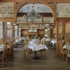 Elegancka restauracja w stylu góralskim, idealna dla hoteli 5 gwiazdkowych. Drewniane zdobienia, kryształowy żyrandol i nakryte stoły tworzą przytulną atmosferę.