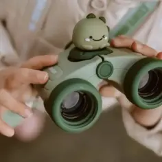 Dziecko trzyma zieloną lornetkę z uroczym dinozaurem. To początek wielkich pasji do odkrywania świata.