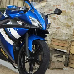 Niebieski sportowy motocykl Yamaha R25, idealny jako pierwszy motor na kat B, stoi na bruku obok drewnianych skrzynek.